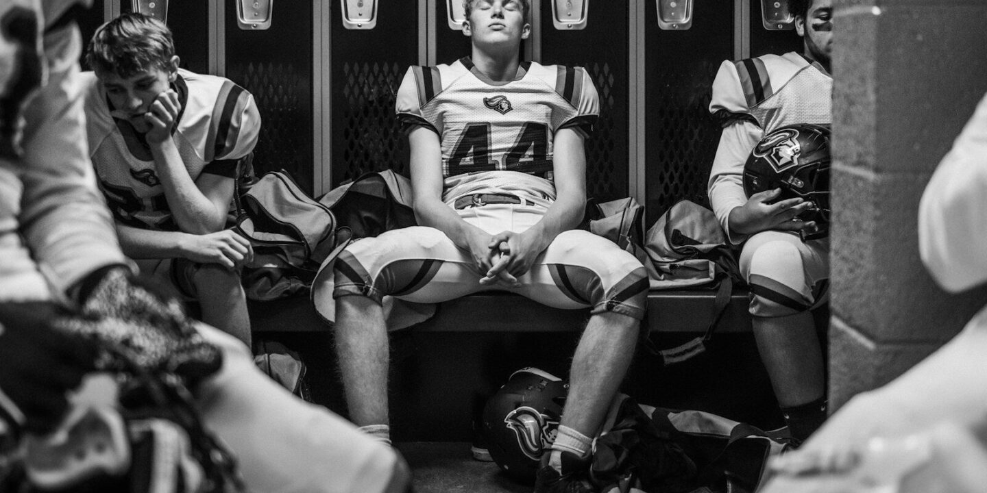 Football players sitting in a locker room.